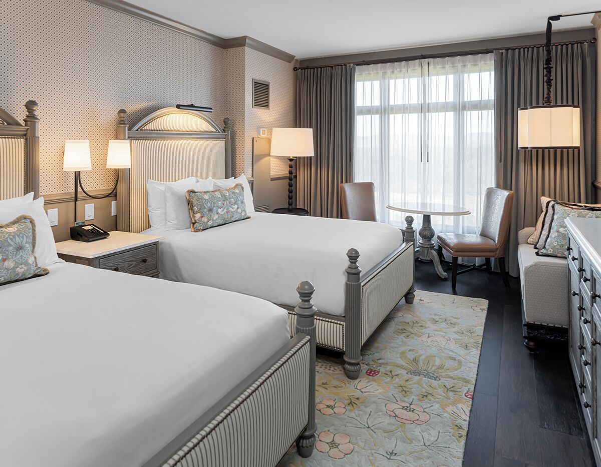 A hotel room with two beds, a desk, a chair, and a dresser.