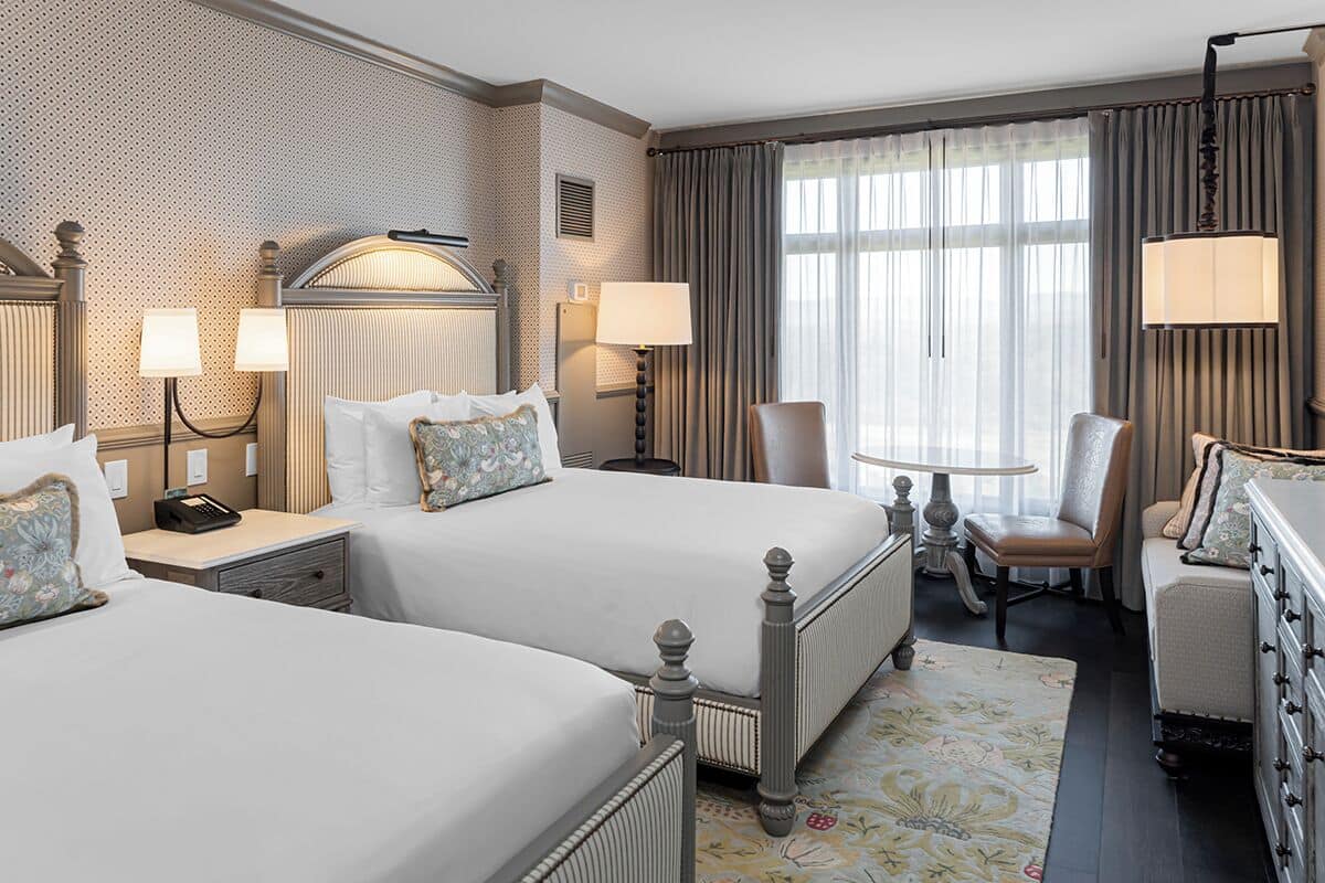 A hotel room with two beds, a desk, a chair, and a dresser.