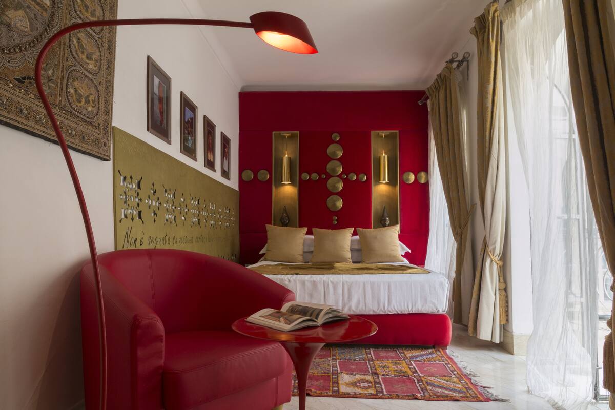 Un dormitorio moderno con un sofá rojo, una mesita con un libro, una pared decorativa y una cama grande con cabecero rojo.