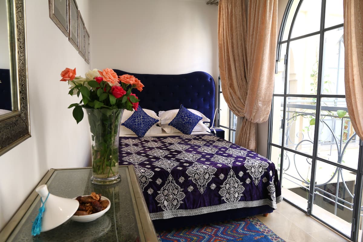 Un dormitorio con cama, un florero con flores, un tazón de nueces y una ventana con cortinas.