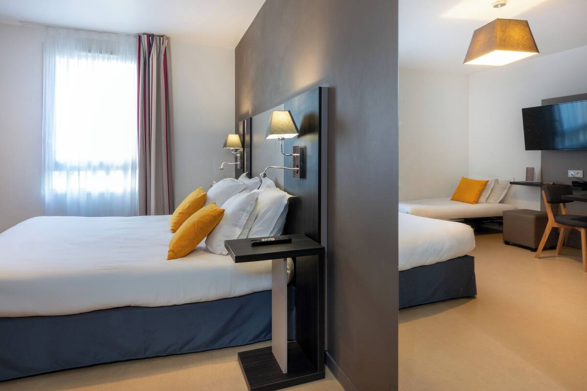 Une chambre d’hôtel moderne équipée de deux lits, d’une télévision et d’un bureau.
