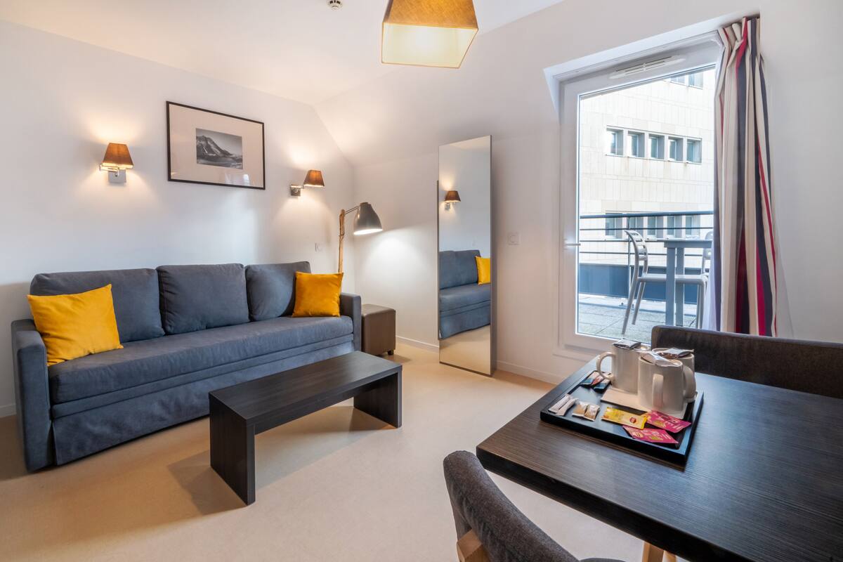 Un salon moderne avec un canapé gris, une table basse et une table à manger sur laquelle se trouve un plateau rempli d’objets.