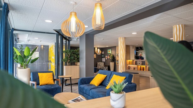 A modern lobby with blue sofas, yellow cushions, and hanging pendant lights.