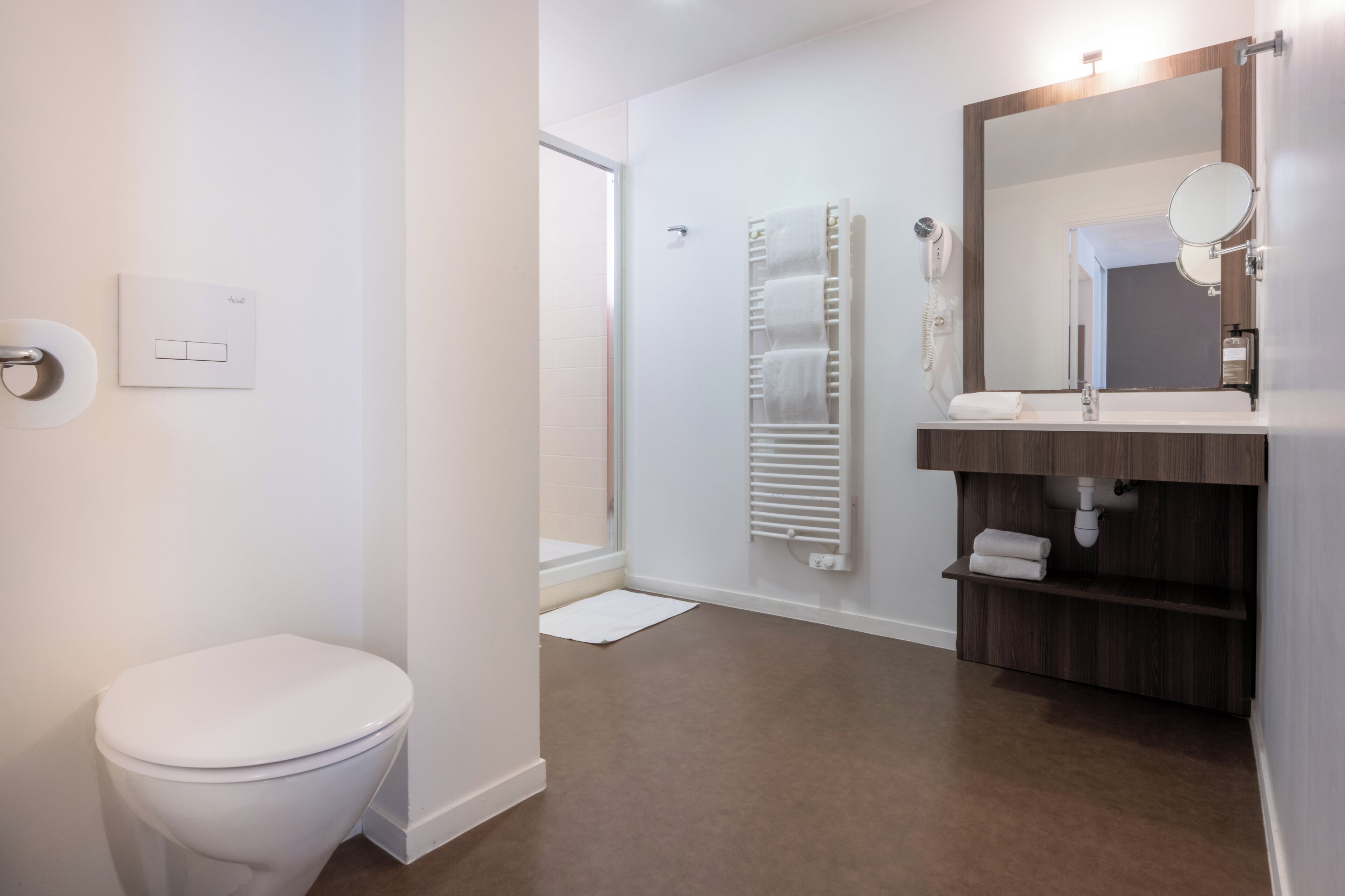 Une salle de bain moderne comprenant des toilettes, une douche, un lavabo avec un miroir et un porte-serviettes.