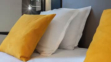 Una cama bien hecha con almohadas blancas y amarillas, una lámpara fijada a la pared y un cabecero oscuro.