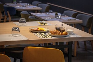 Uma sala de jantar com mesas preparadas para o café da manhã, incluindo pratos de ovos, croissants e um copo de leite.