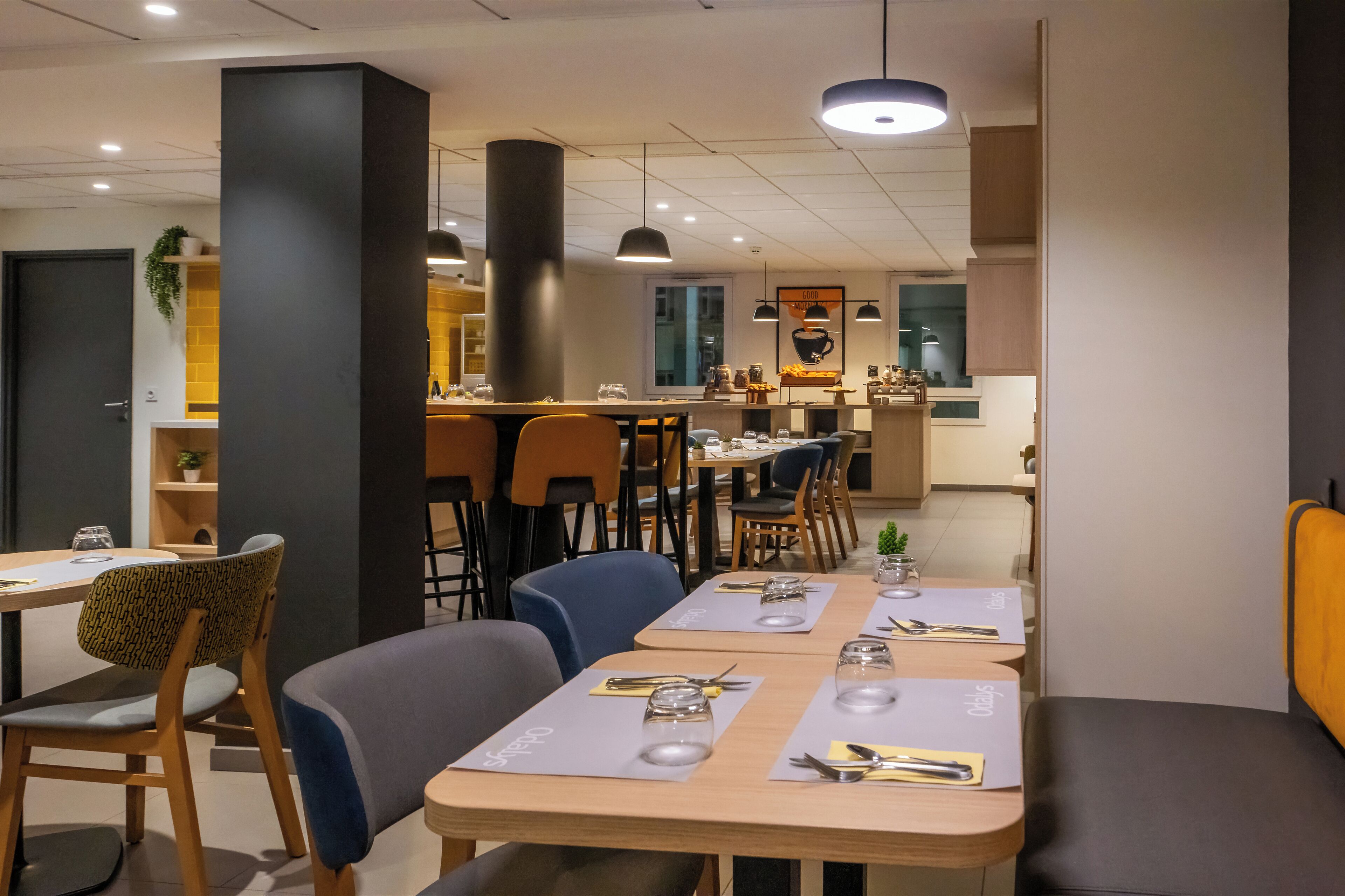 A modern restaurant interior with wooden tables, cushioned chairs, and pendant lighting.