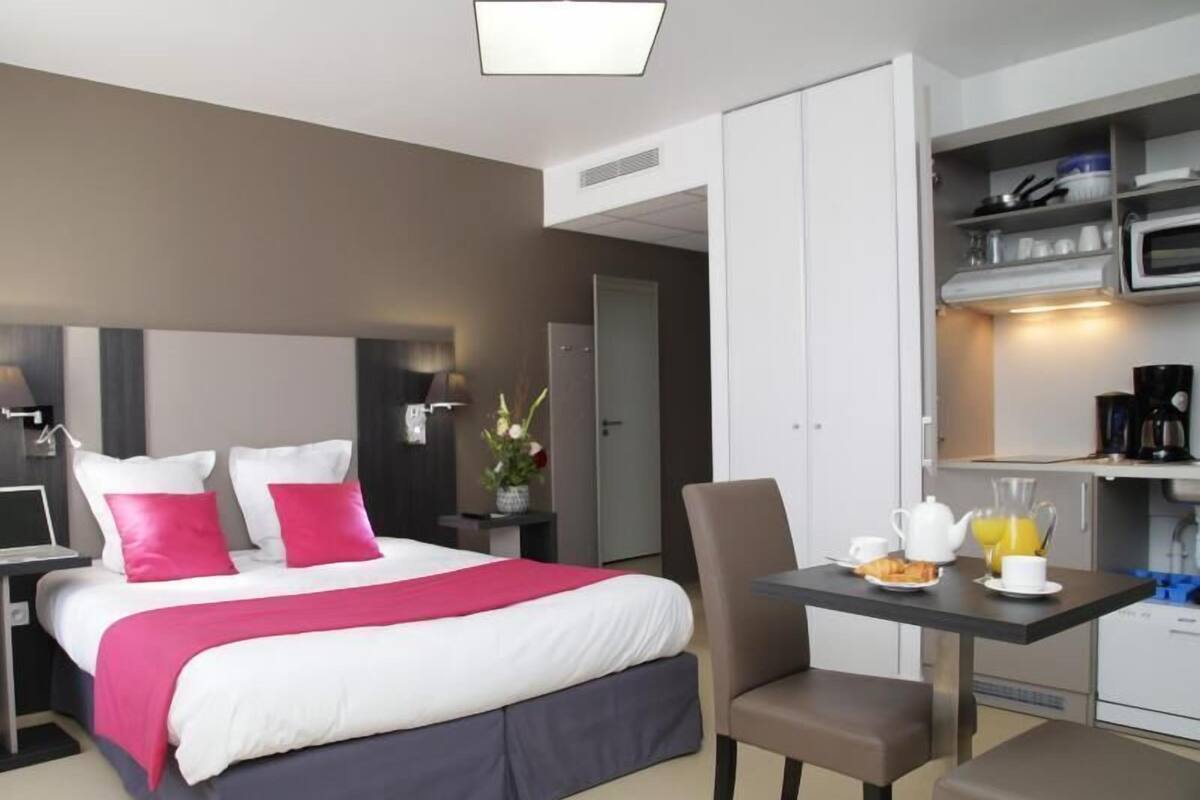 Une chambre d’hôtel comprenant un lit, une table de chevet, une chaise, un bureau et une kitchenette.