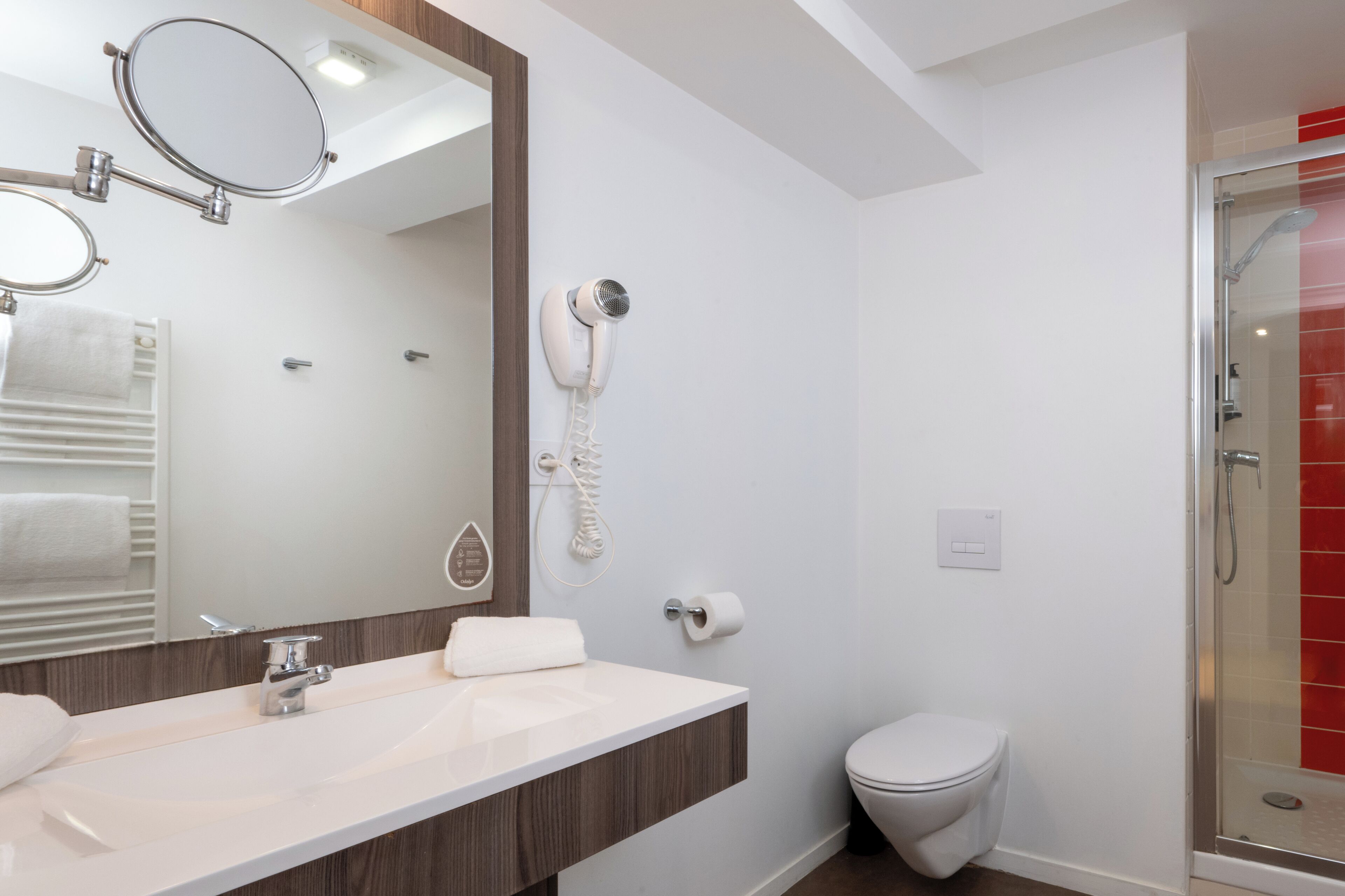 Un baño moderno con lavamanos blanco, espejo, secador de pelo, inodoro y ducha.