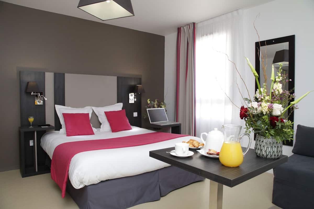 A hotel room with a bed, a desk with breakfast items, a laptop, and a large window with curtains.