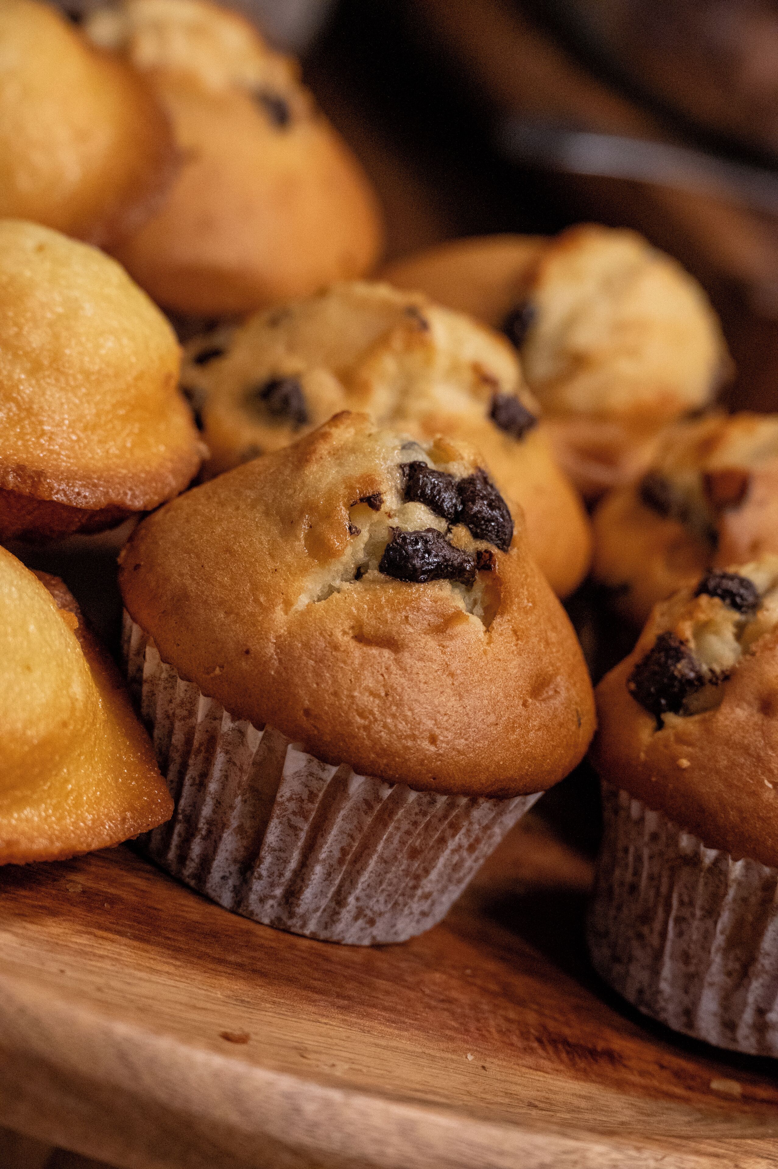 A wooden tray with several muffins in paper liners.