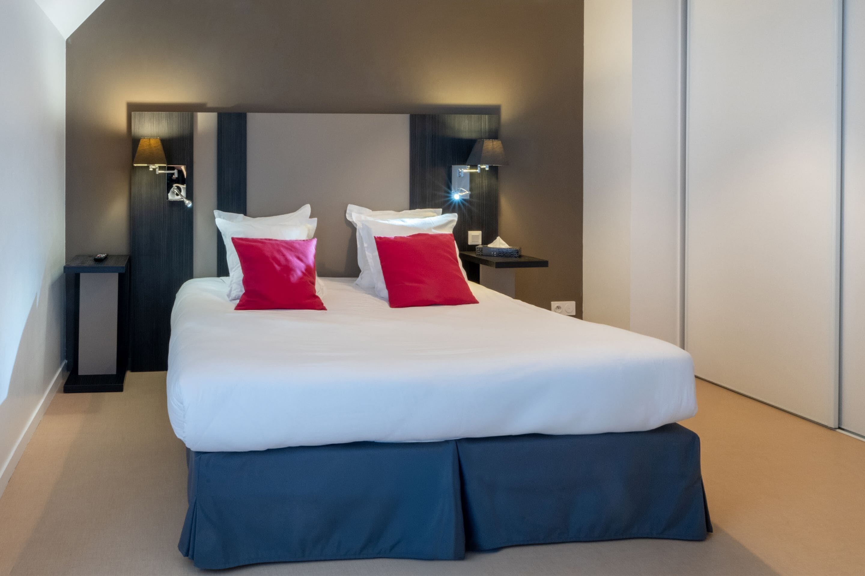 Una habitación de hotel moderna con una cama grande, dos mesitas de noche con lámparas y un cabecero oscuro.