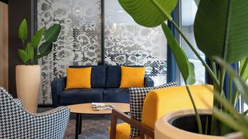 Uma área de estar moderna com sofá, poltronas estampadas, mesa de centro e uma grande planta em vaso.