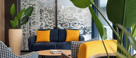 A modern lounge area with a sofa set, patterned chairs, a coffee table, and a large potted plant.