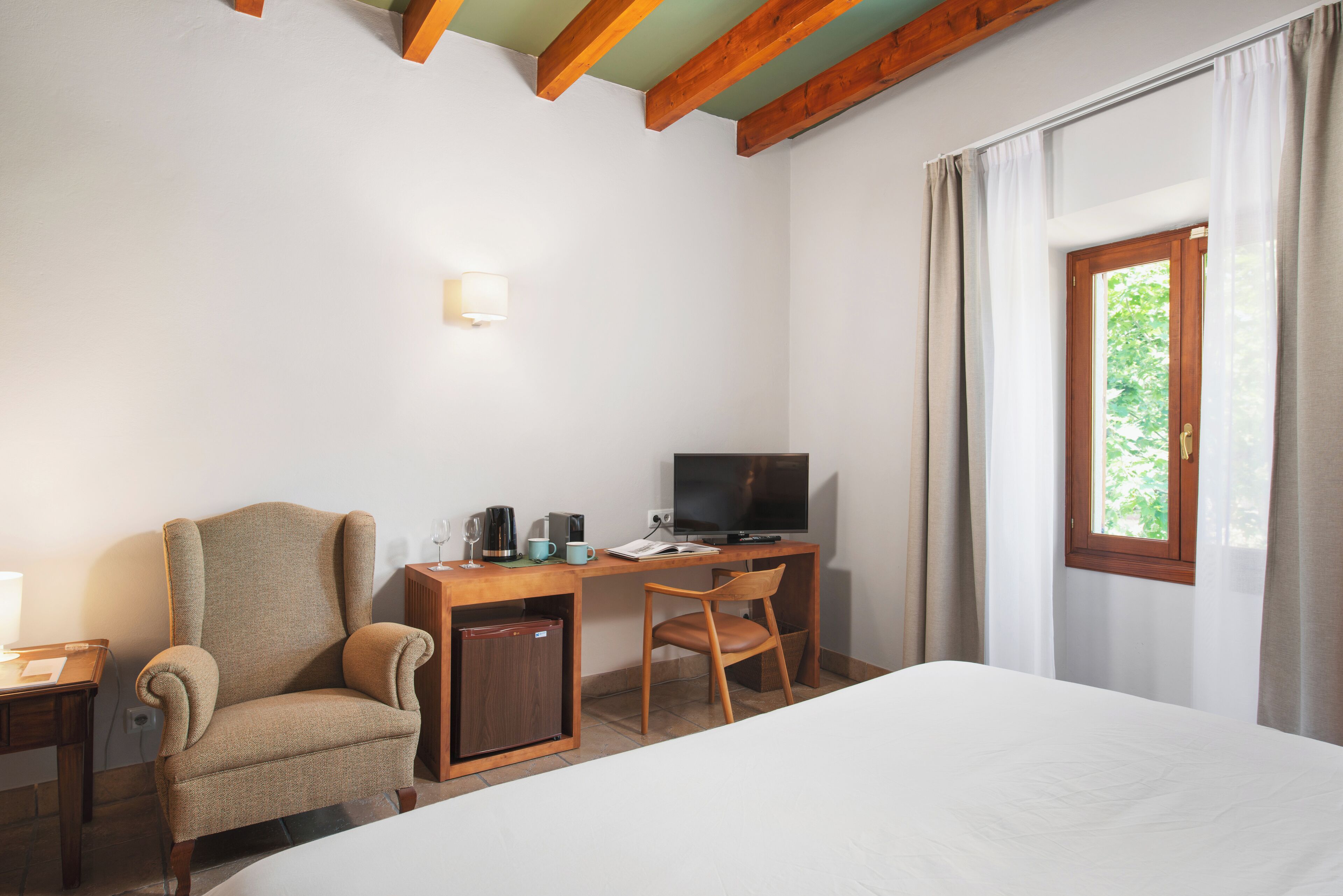 A hotel room with a bed, a desk with a television, a chair, and a small cabinet.