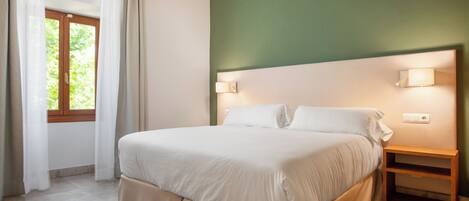 A bedroom with a bed, a nightstand, a window with curtains, and a wall-mounted light fixture.