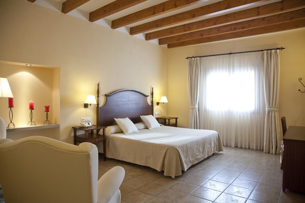 Una habitació d'hotel amb un llit, taules de nit, làmpades, una cadira i una finestra amb cortines.