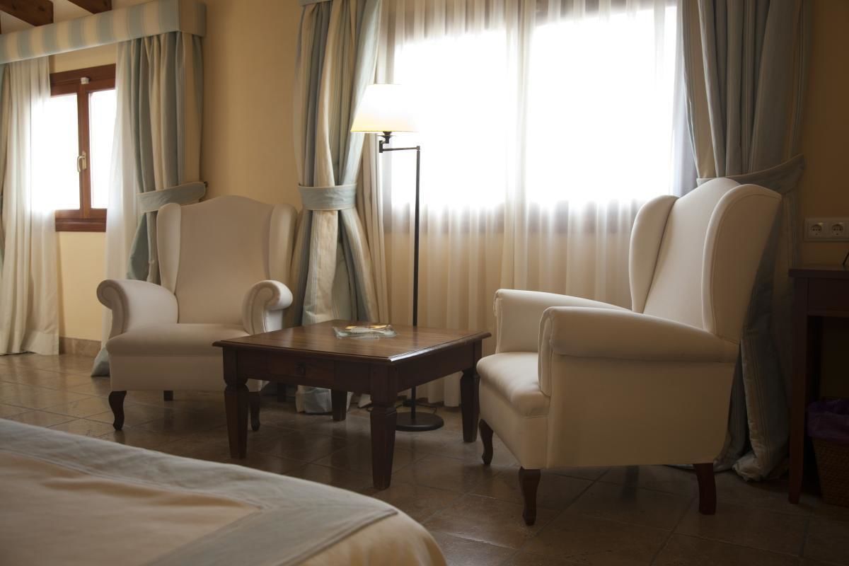 A hotel room with two armchairs, a small table, and a lamp.