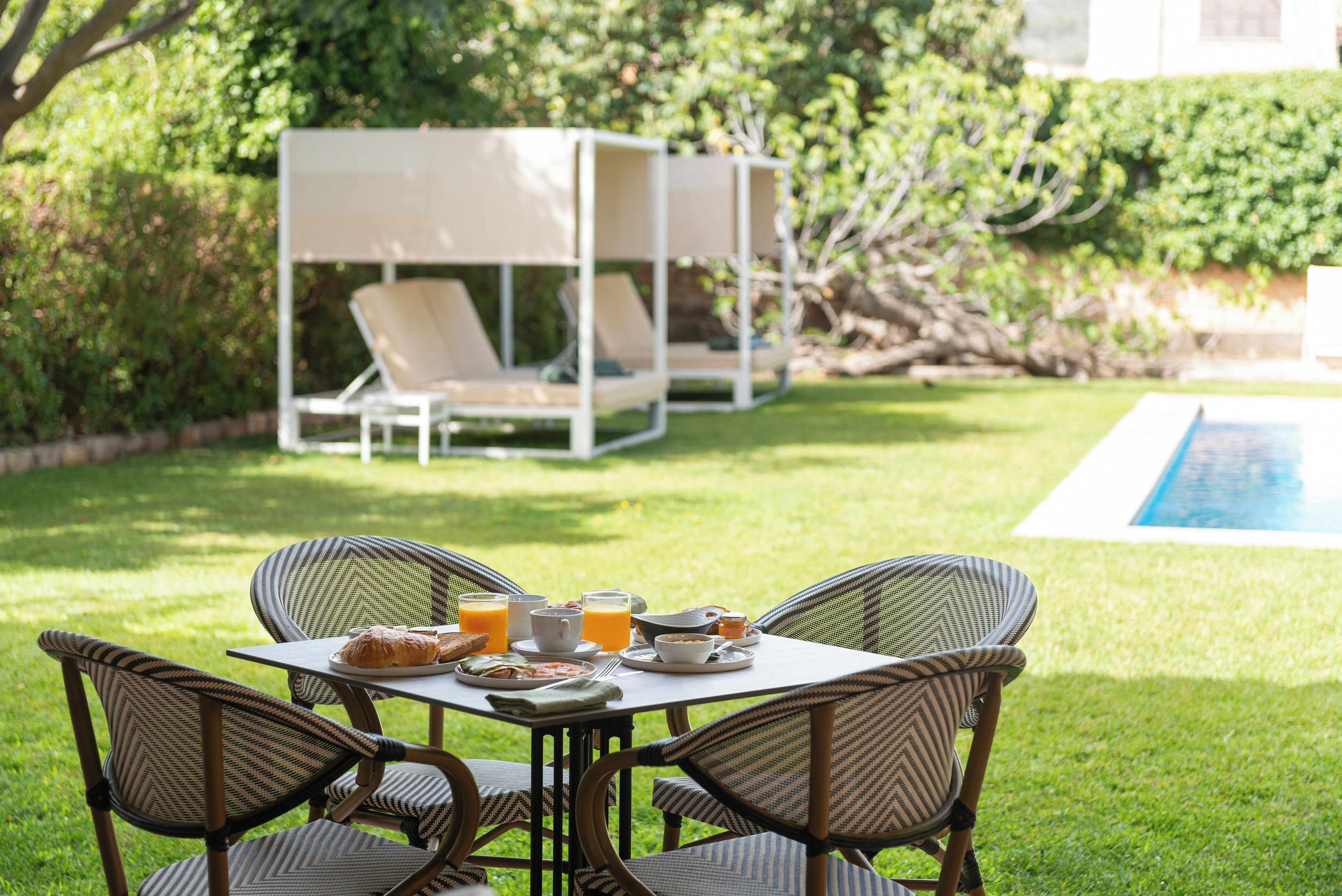 An outdoor dining area with a table set for breakfast, surrounded by wicker chairs, and a white canopy structure in the background.