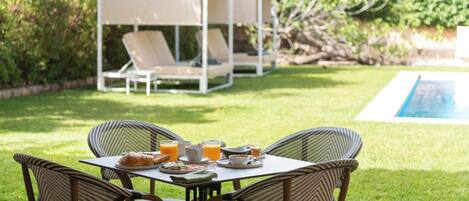 An outdoor dining area with a table set for breakfast, surrounded by wicker chairs, and a white canopy structure in the background.