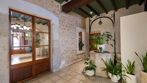 Un hall d’entrée spacieux avec un mur en pierre, une porte en bois, un sol carrelé et des plantes en pot.