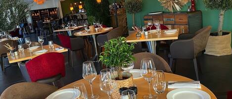 Ein Restaurant mit runden Tischen, gedeckten Plätzen, klarem Glas und Geschirr, sowie einer grünen Wand mit einem dekorativen Kranz und dem Schriftzug "Amore".
