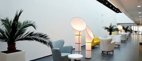 A modern lobby with seating areas, a large potted plant, and a unique floor lamp.