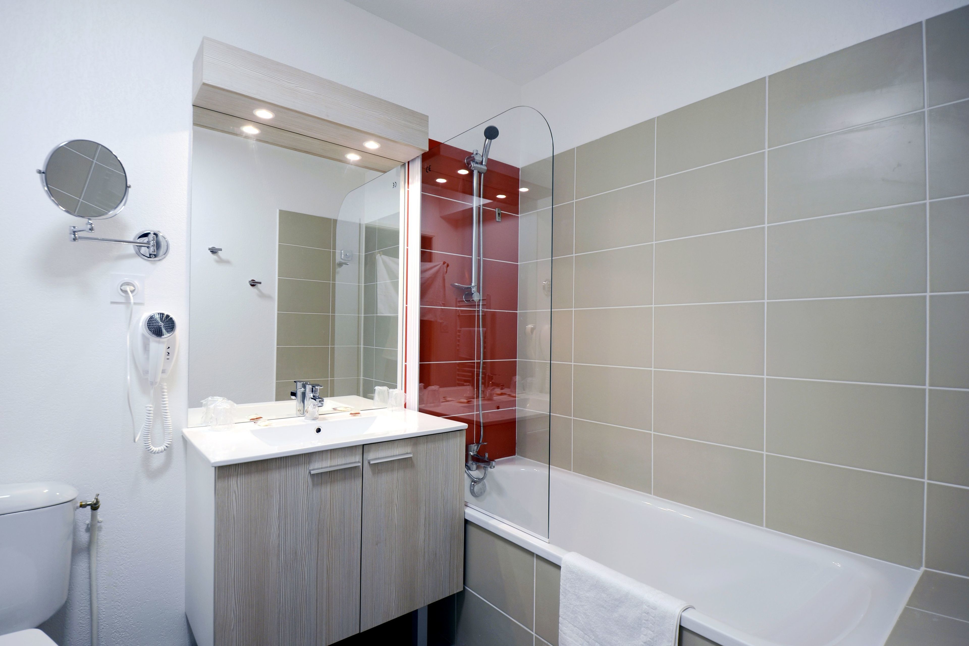 Un bagno moderno con lavandino bianco, uno specchio, un soffione doccia a mano e una vasca da bagno.