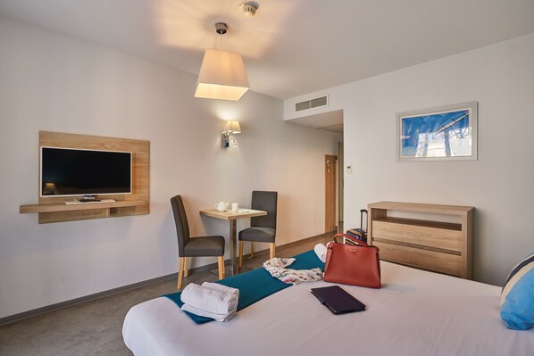 A hotel room with a bed, a TV, a desk, and a chair.