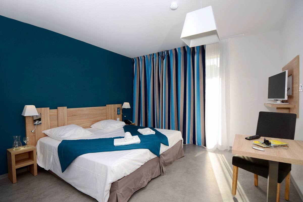 A hotel room with a bed, bedside tables, a desk, a chair, and a television.