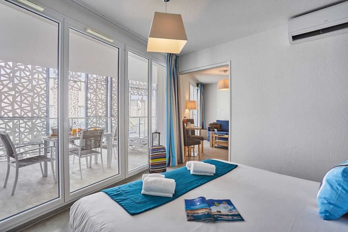 A hotel room with a large bed, a view to the outside, a desk, and a chair.