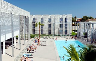 Zona de piscina con sillas de descanso y una pileta, rodeada de edificios modernos con fachadas decoradas.