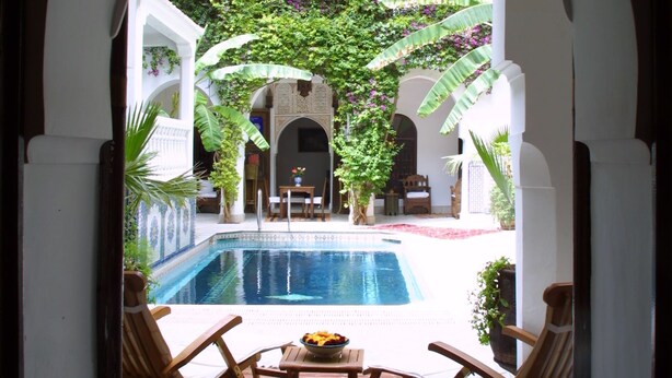 An indoor pool area with a view of a lush garden through an arched doorway. - Riad Dar El Assafir (Marrakech)