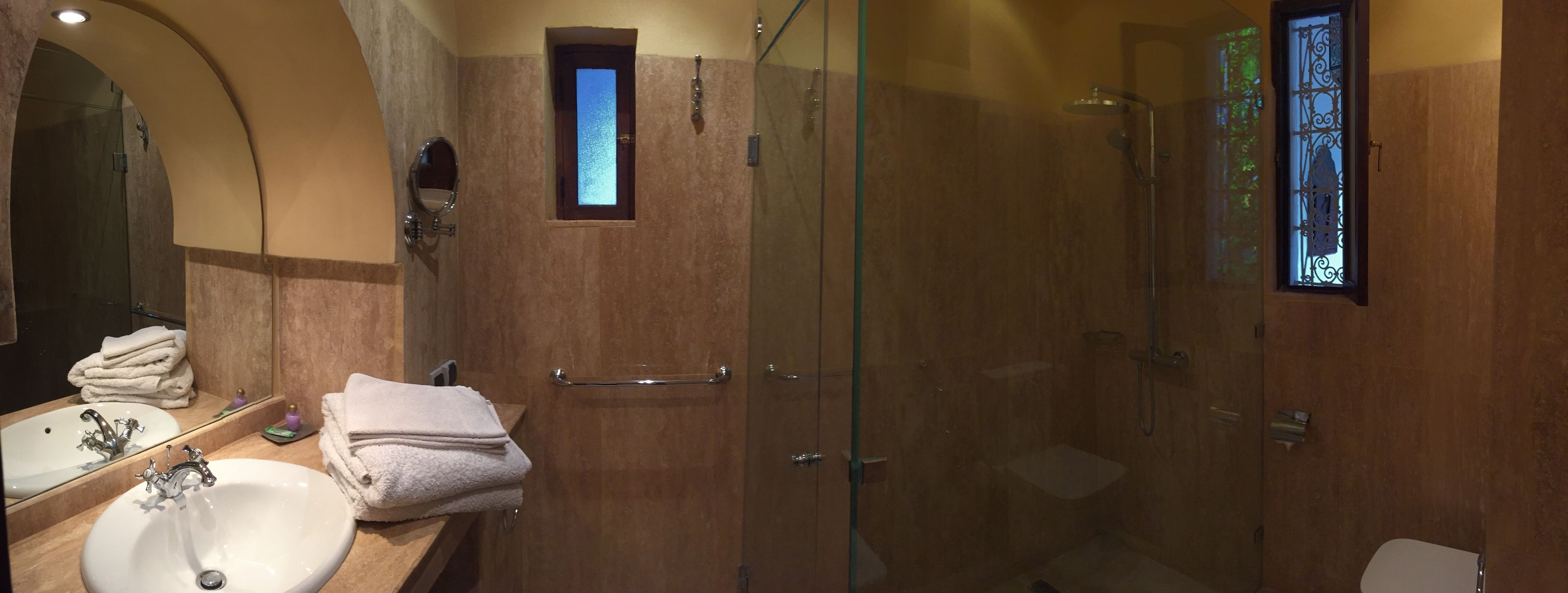 A bathroom with a glass-enclosed shower, a sink with a mirror, and a small window.