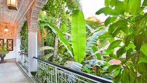 An indoor garden with a white railing, large green leaves, and intricate ceiling patterns. - Riad Dar El Assafir (Marrakech)