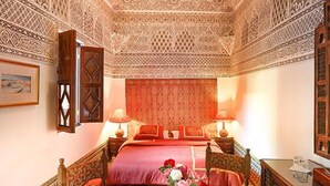 A room with a bed, two bedside tables, a chair, a small table with a vase of flowers, and a decorative ceiling. - Riad Dar El Assafir (Marrakech)