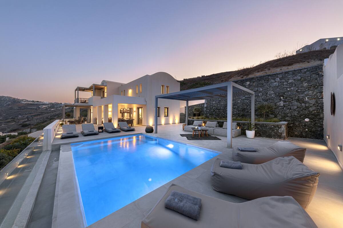 A modern villa with a swimming pool, outdoor seating, and a stone wall.
