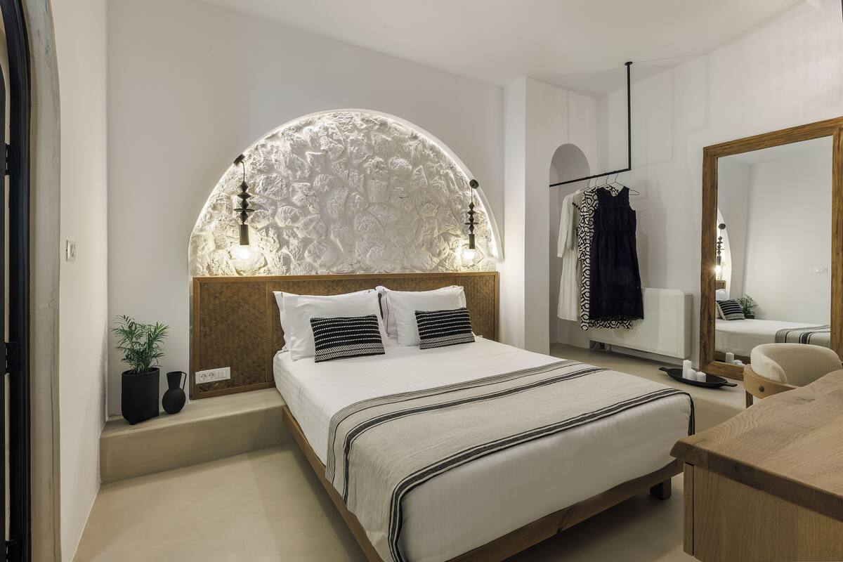 A modern bedroom with a large bed, a curved wall headboard, a mirror, and a wooden desk.