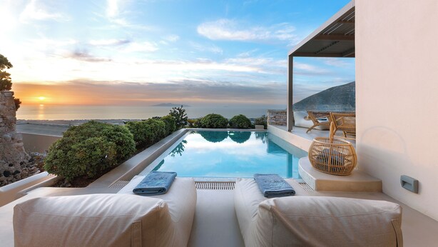 Piscina privada con sillones de descanso y vista a la puesta de sol sobre el océano.