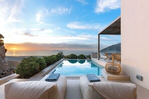 A private pool with lounge chairs and a view of the sunset over the ocean. - Eolia Luxury Villas (Santorini)
