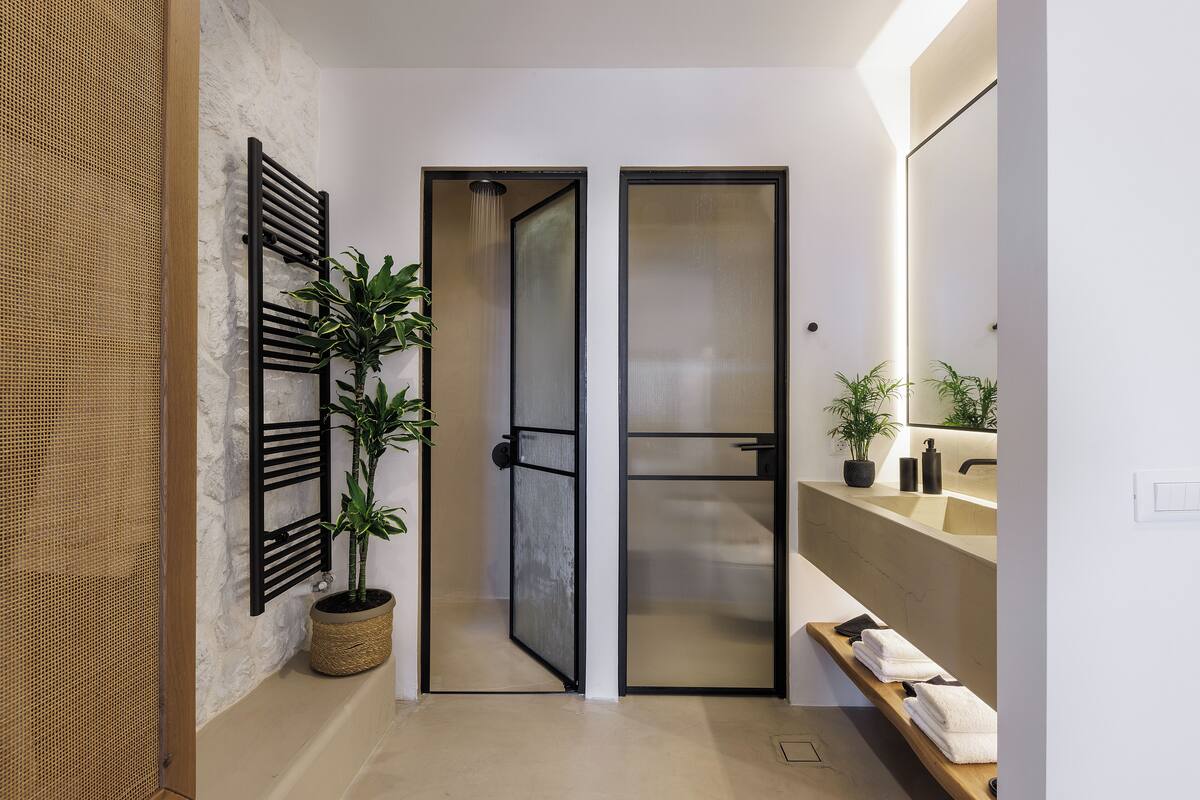 A modern bathroom with a shower, a sink, and a mirror. There are plants and towels on the counter.