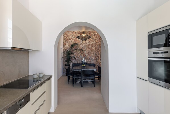 A modern kitchen with a stone wall arch, built-in appliances, and a dining area with a table and chairs.