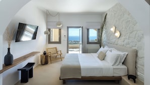 Un dormitorio con cama, televisión, banca, silla y vista al mar.