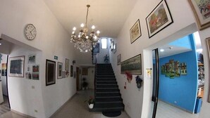 A hallway with a staircase, framed pictures, and a chandelier. - Hotel Sorrento (Jesolo)