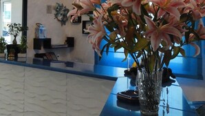 A reception area with a large, textured ceiling, a blue counter, and a vase of pink lilies. - Hotel Sorrento (Jesolo)