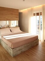 A modern bedroom with a large bed, wooden headboard, and a view of the city through a large window.