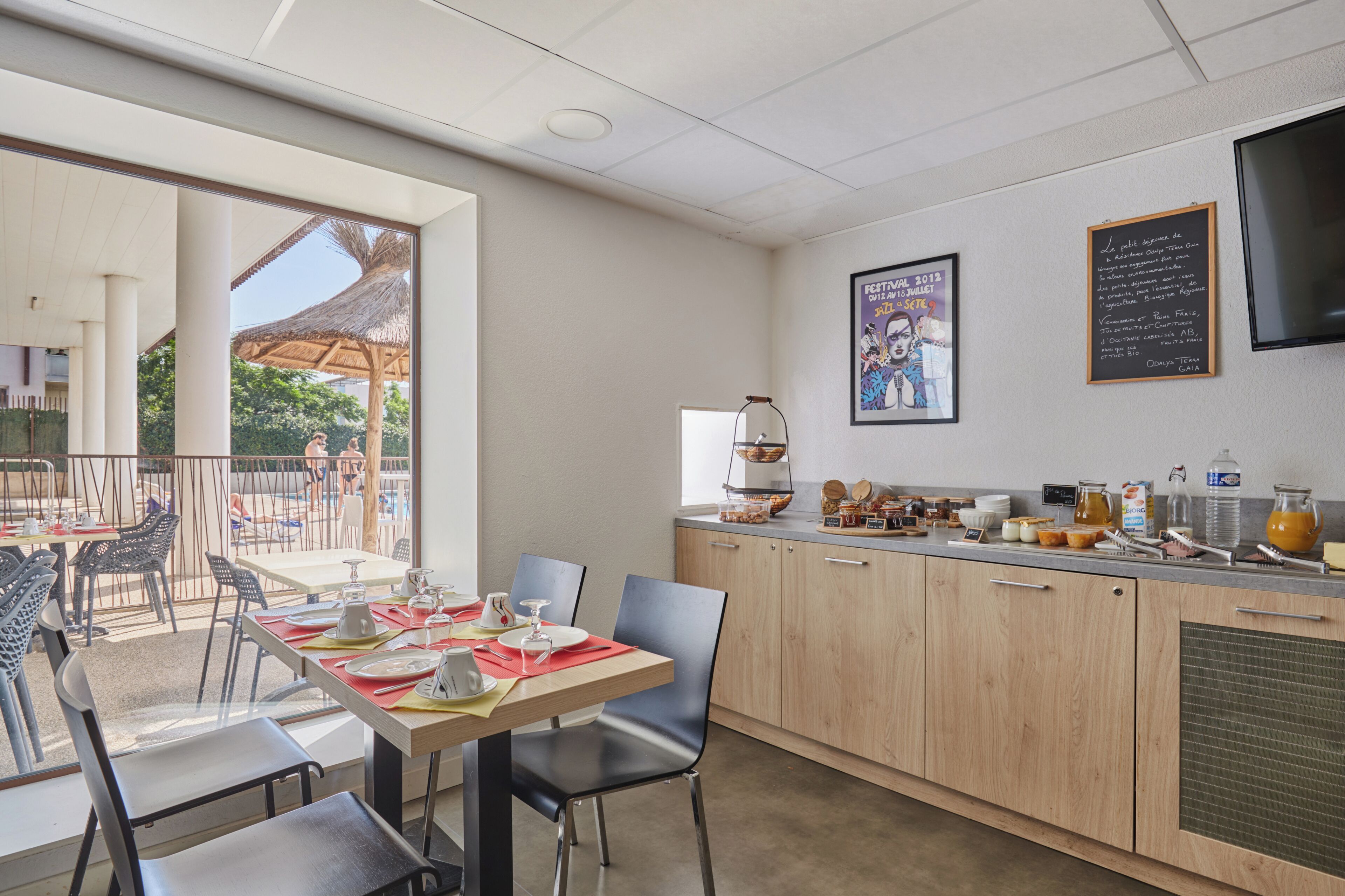 Un bar où l’on peut prendre le petit-déjeuner, avec des sièges, un tableau noir servant de menu et une vue sur l’espace extérieur aménagé pour les clients.