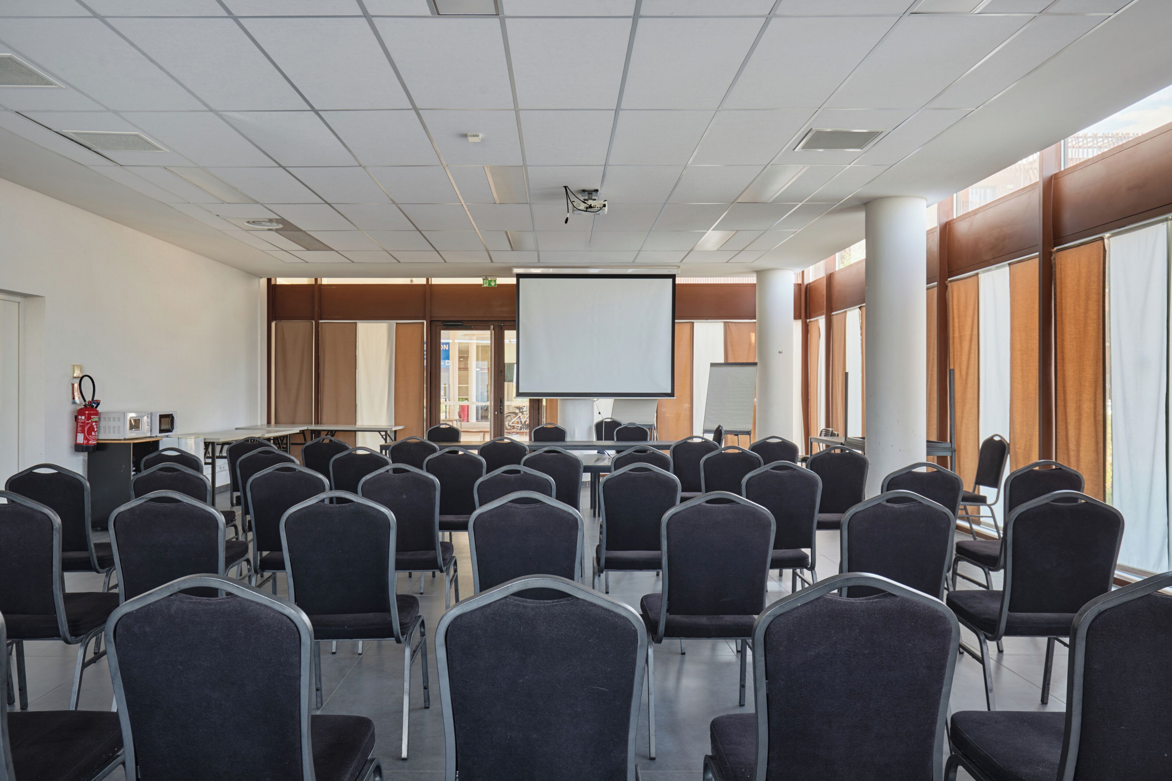 Une salle de conférence avec des rangées de chaises, un écran de projection et un tableau blanc.