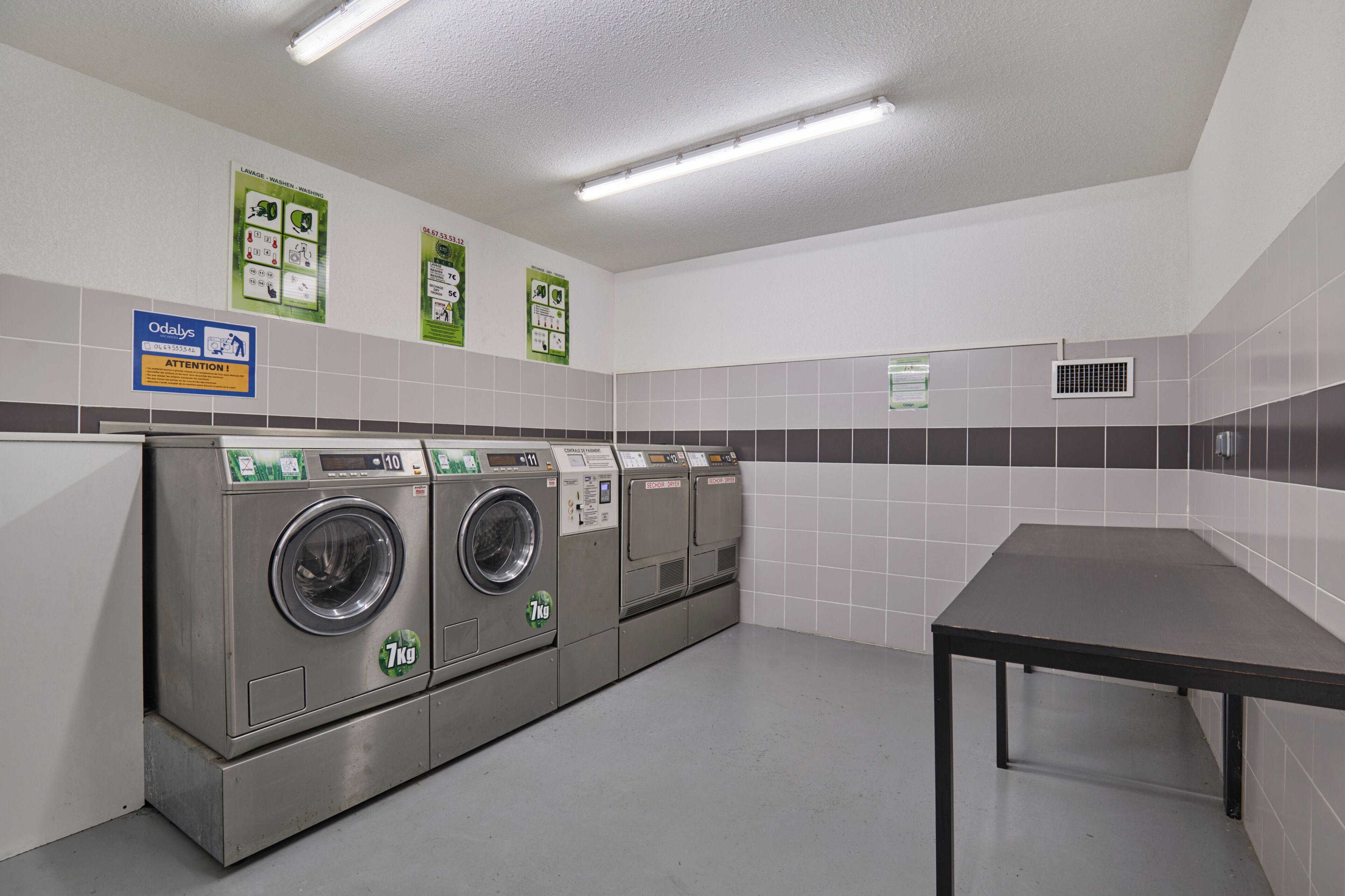 A laundry facility with multiple washing machines, a table, and informational signs on the walls.