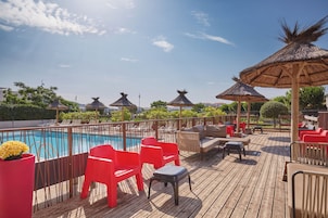 A wooden deck with a pool, red chairs, and thatched umbrellas.